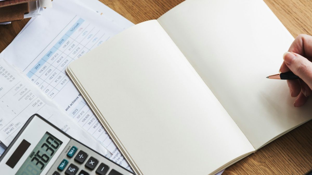 Personne calculant ses heures de travail avec une calculatrice et des documents comptables sur un bureau