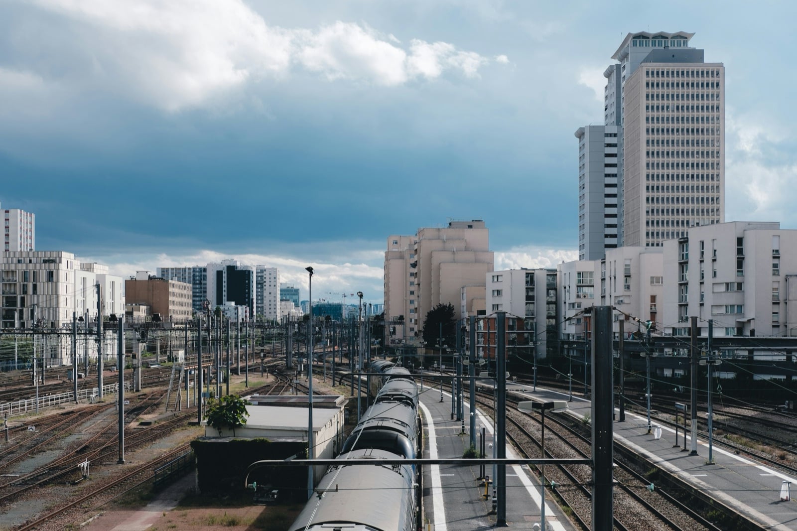 Voies de la gare Montparnasse côté Vaugirard, un train à quai et des immeubles de bureaux sous un ciel d'orage