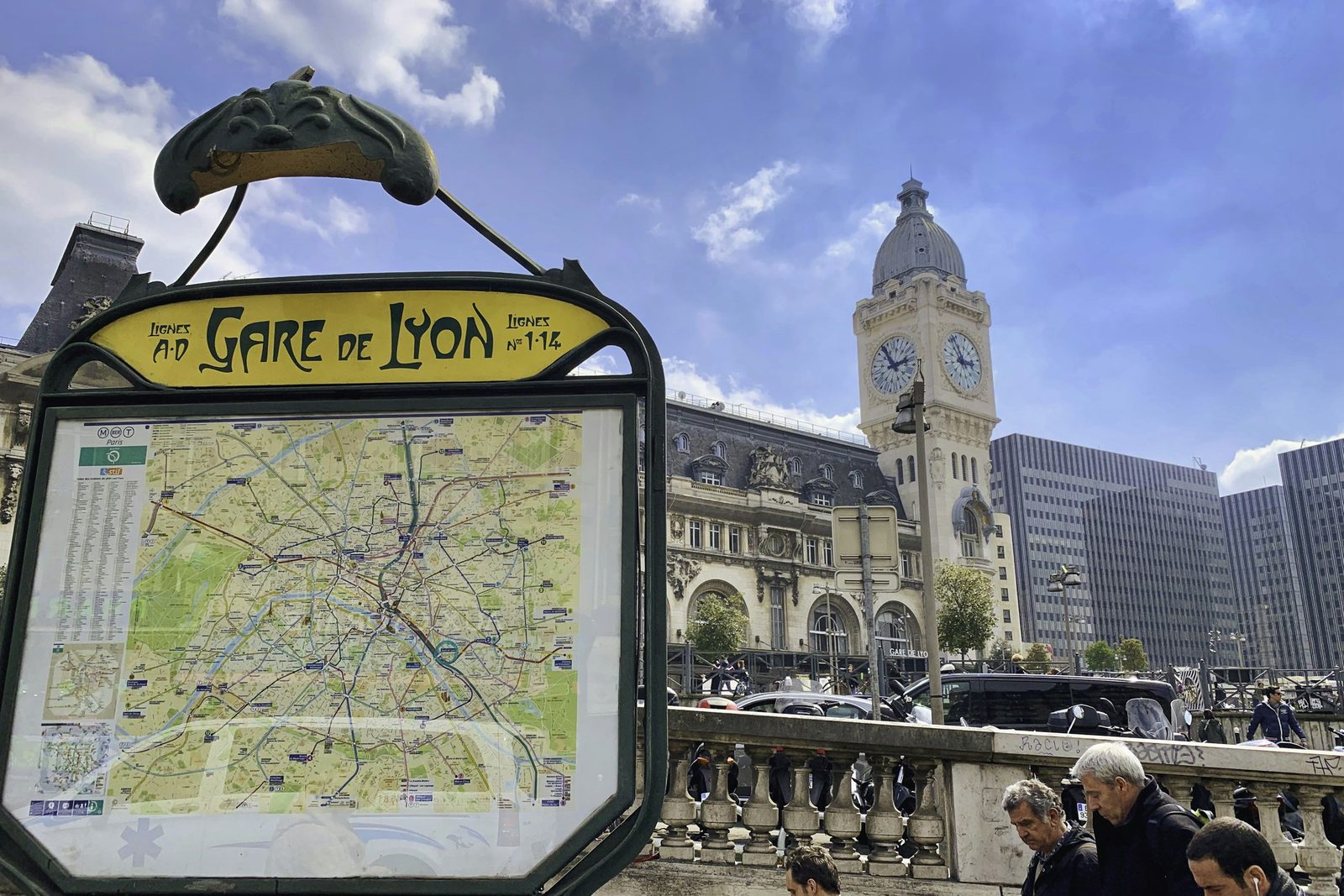 Plan du métro sous l'enseigne « Gare de Lyon, lignes 1 et 14 », devant la tour de l'horloge de la gare de Lyon et des passants