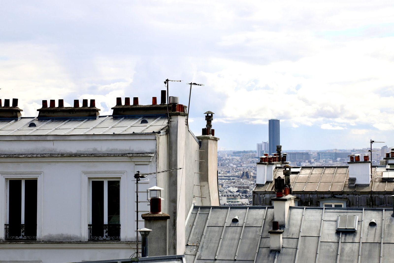 Toits en zinc et chambres sous les combles d'un immeuble parisien, la tour Montparnasse à l'horizon
